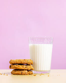 Raisin cookies stacked near glass of milk against pink colored background - FLMF01034