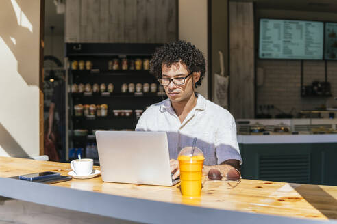 Junger Freiberufler mit Laptop am Tisch im Café - PBTF00340