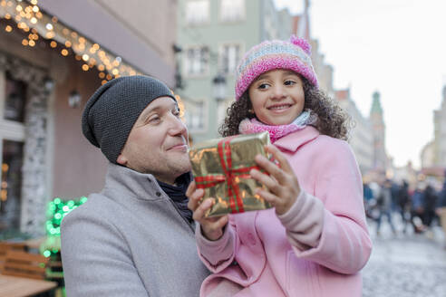 Lächelnder Vater mit Tochter und Geschenk auf dem Weihnachtsmarkt - VIVF01084