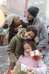 Glückliche Eltern mit Kindern, die auf dem Weihnachtsmarkt Geschenkboxen halten - VIVF01094