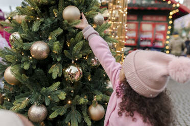 Mädchen berührt Weihnachtsschmuck am Baum auf dem Markt - VIVF01095