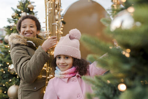 Glückliche Geschwister, die sich in der Nähe von Weihnachtsbäumen vergnügen - VIVF01097