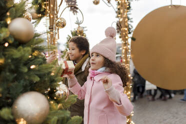 Glückliches Mädchen, das eine Geschenkbox hält und sich mit seinem Bruder auf dem Weihnachtsmarkt freut - VIVF01099