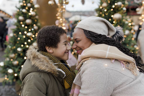 Lächelnde Mutter reibt sich mit ihrem Sohn auf dem Weihnachtsmarkt die Nasen - VIVF01102