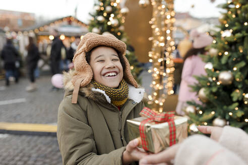 Die Hände einer Frau, die einem Jungen auf dem Weihnachtsmarkt ein Geschenk überreicht - VIVF01104