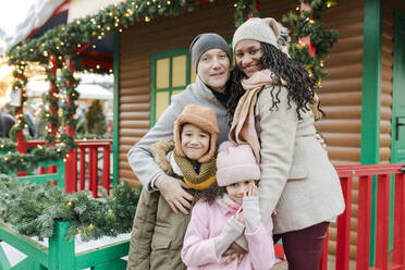 Glückliche Familie vor einem Holzhaus auf dem Weihnachtsmarkt - VIVF01106