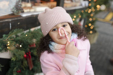 Lächelndes Mädchen mit Zuckerstange im Gesicht auf dem Weihnachtsmarkt - VIVF01107