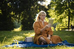 Lächelnde Frau sitzt auf einer Decke und benutzt einen Tablet-PC im Park - JOSEF21465