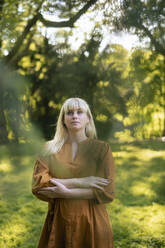 Thoughtful woman standing with arms crossed in park - JOSEF21477