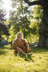 Contemplative woman sitting on grass in park - JOSEF21480