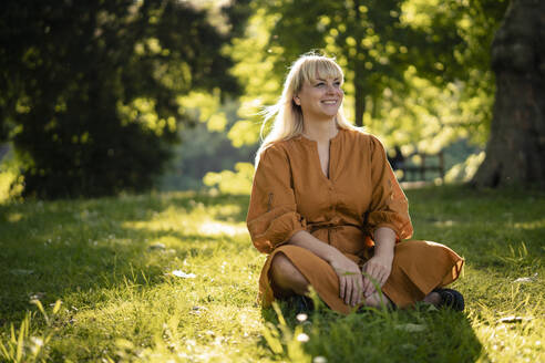 Glückliche blonde Frau sitzt auf Gras im Park - JOSEF21482