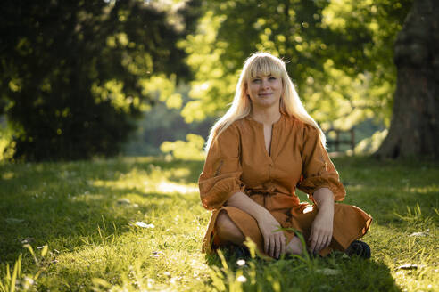 Lächelnde blonde Frau sitzt im Gras - JOSEF21483