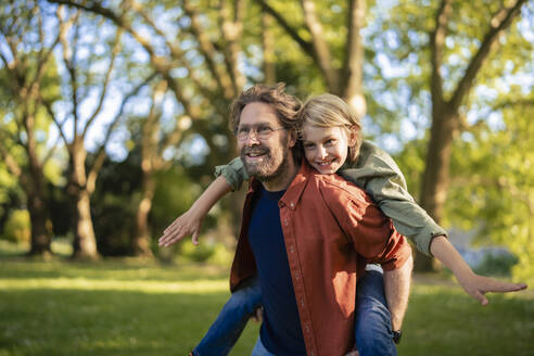 Smiling father giving piggyback ride to son in park - JOSEF21487