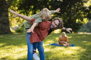 Smiling father having fun and playing with son in park - JOSEF21493