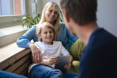 Vater und Mutter mit Sohn, der zu Hause einen Tablet-PC hält - JOSEF21519