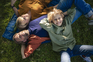 Smiling boy lying with father and mother in park - JOSEF21526