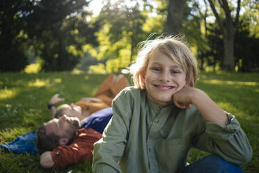 Smiling boy with parents in background relaxing in park - JOSEF21531