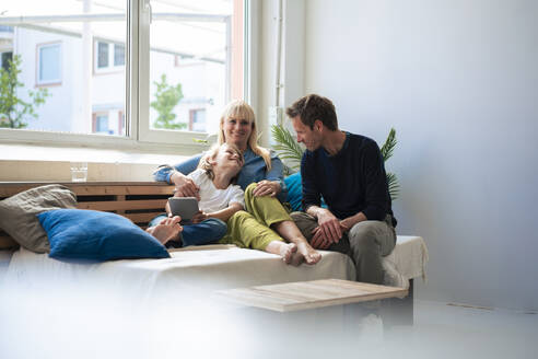 Happy parents with son sitting on sofa at home - JOSEF21534