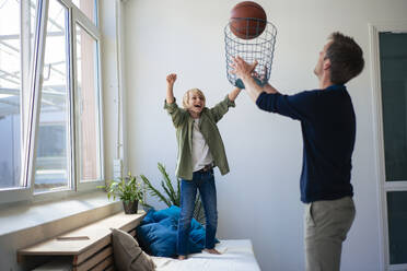 Glücklicher Sohn und Vater spielen Basketball mit Papierkorb zu Hause - JOSEF21554