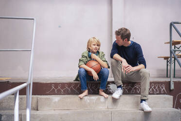 Vater sitzt mit Sohn, der einen Basketball hält, auf einer Treppe - JOSEF21562