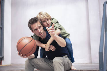 Father holding basketball and gesturing with son in front of wall - JOSEF21566