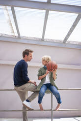 Vater spricht mit Sohn, der Basketball hält und auf dem Geländer sitzt - JOSEF21571