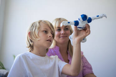 Lächelnde Mutter und Sohn spielen mit Roboter zu Hause - JOSEF21580