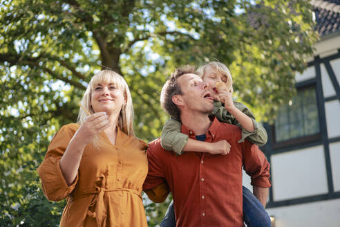 Smiling mother with father giving piggyback ride to son eating ice cream - JOSEF21589