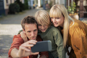 Smiling father taking selfie with woman and son through smart phone - JOSEF21598