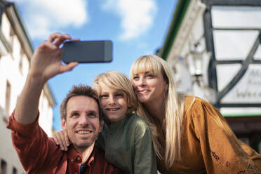 Happy father taking selfie with woman and son through smart phone near buildings - JOSEF21599