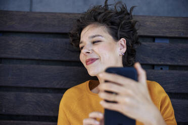 Smiling woman lying on bench with smart phone - JOSEF21604