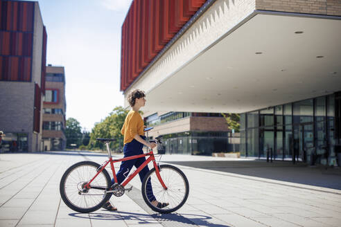 Junge Frau zu Fuß mit Fahrrad an einem sonnigen Tag - JOSEF21615