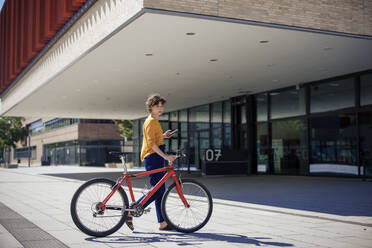 Junge Frau zu Fuß mit Fahrrad in der Nähe eines Gebäudes - JOSEF21616