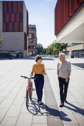 Smiling woman talking and walking with senior man on sunny day - JOSEF21618