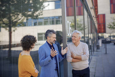Senior businessman explaining and having discussion with colleagues near glass wall - JOSEF21626