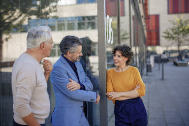 Smiling businesswoman talking with colleagues near building - JOSEF21628