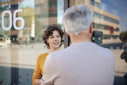 Lächelnde junge Geschäftsfrau im Gespräch mit einem Kollegen an einer Glaswand - JOSEF21643