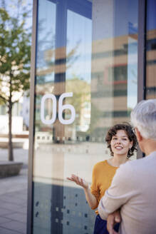 Smiling businesswoman talking to senior colleague near glass wall - JOSEF21645