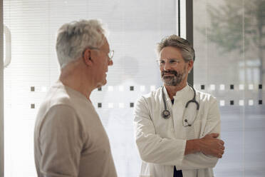 Smiling senior doctor talking to man near glass - JOSEF21658