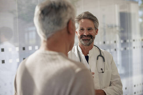 Lächelnder Oberarzt im Gespräch mit einem Mann im Krankenhaus - JOSEF21662
