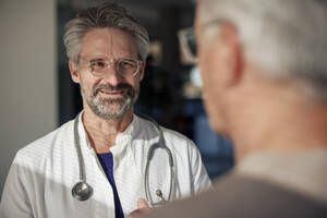 Lächelnder Oberarzt im Gespräch mit einem Mann im Krankenhaus - JOSEF21667