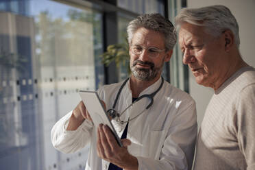 Senior doctor discussing with man over tablet PC in hospital - JOSEF21670