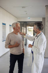 Doctor consoling man standing in hospital corridor - JOSEF21674