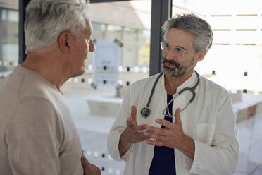 Senior doctor gesturing and explaining to man near glass window - JOSEF21675