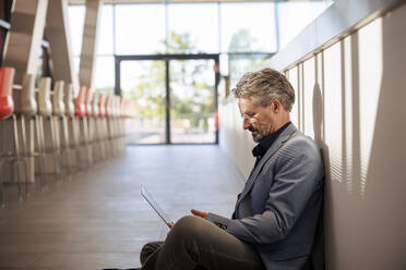 Businessman working on laptop and sitting near wall in cafeteria - JOSEF21702