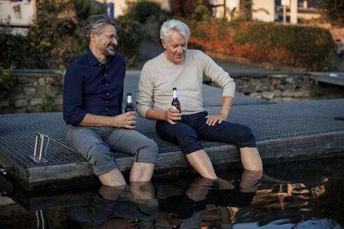 Happy senior friends sitting on pier with beer bottles - JOSEF21712