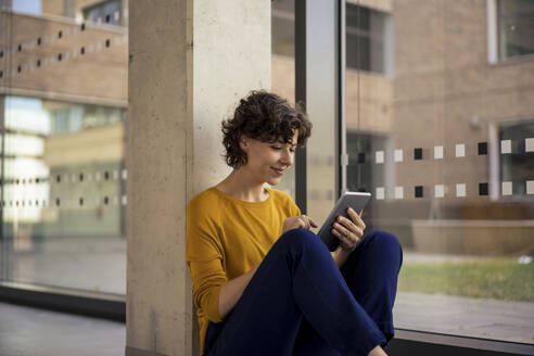Lächelnde Geschäftsfrau mit Tablet-PC in der Nähe eines Glasfensters - JOSEF21734