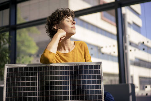 Geschäftsfrau sitzend mit geschlossenen Augen und Sonnenkollektor im Büro - JOSEF21766