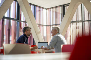 Ältere Geschäftsleute diskutieren und sitzen mit Laptop am Tisch in der Büro-Cafeteria - JOSEF21803
