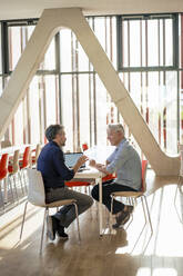 Ältere Geschäftsleute diskutieren und sitzen mit Laptop in der Büro-Cafeteria - JOSEF21804
